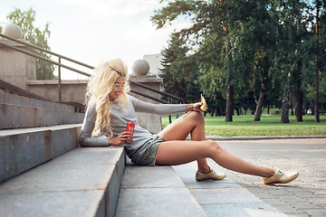 Image showing beauty blonde young woman sitting on outdoor and eating