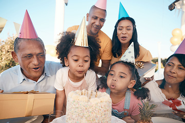 Image showing Family, birthday and girl is blowing candles with party hats for celebration at house for fun. Happiness, kid and make a wish with cake or children, grandparents for special event in outdoor.