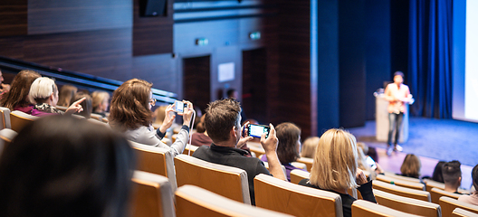 Image showing Speaker giving a talk in conference hall at business event. Rear view of unrecognizable people in audience at the conference hall. Business and entrepreneurship concept.