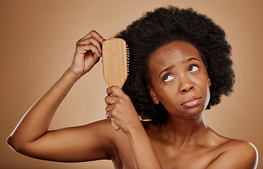 Image showing Black woman, hair care and worry with brush in studio, brown background and curly afro. Beauty, sad female model and comb tangled knot in hairstyle with anxiety, stress and unhappy with dry texture