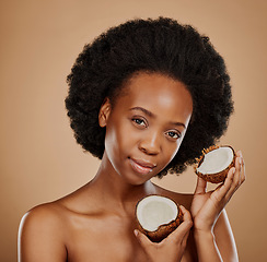 Image showing Portrait, facial and coconut with a model black woman in studio on a brown background for natural treatment. Face, skincare or luxury beauty cosmetics with a young female person holding fruit for oil