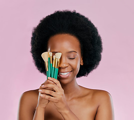 Image showing Face, makeup and black woman with brushes, eyes closed and smile in studio isolated on a pink background. Skincare, facial cosmetics and African model with tools for foundation, powder and beauty.