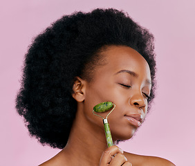 Image showing Facial roller, massage and black woman with natural beauty, face care and skin glow on pink background. Female model, cosmetic tools and dermatology with jade crystal, afro hairstyle and skincare