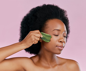 Image showing Gua sha, massage and black woman with natural beauty, face care and skin glow on pink background. Female model, jade cosmetic tools and dermatology with afro hair and facial skincare in studio