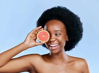 Image showing Skincare, woman and grapefruit on eye for beauty, cosmetics and natural product, health or vitamin c promotion. Happy African person or model with red fruit for dermatology on studio blue background