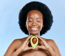 Image showing Face, beauty and avocado with a black woman on a blue background in studio to detox for wellness. Skincare, smile and eyes closed with a happy young female model holding a fruit for antioxidants