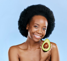 Image showing Portrait, beauty and avocado with a black woman on a blue background in studio to detox for wellness. Skincare, smile and face with a happy young female model holding a fruit for antioxidants