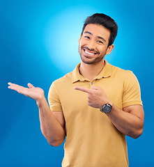 Image showing Portrait, man or palm for advertising space, mockup or product placement in studio, blue background or promotion deal. Happy asian, male model and pointing to presentation, information or news review