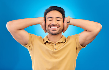 Image showing Sound, silence and man cover ears, noise and happiness against a blue studio background. Male person, guy and model silent, gesture and quiet with a smile, happy and relax with peace, calm and joyful