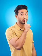 Image showing Asian man, secret and finger on lips in studio for privacy, mystery and sale announcement on blue background. Male model, silence and shush for quiet, gossip or whisper emoji of confidential surprise