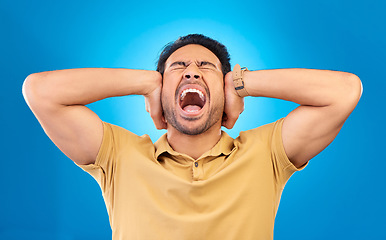 Image showing Man cover his ears while shouting in a studio for angry, upset or mad argument expression. Crazy, scream and young male person with an open mouth for loud voice gesture isolated by a blue background.