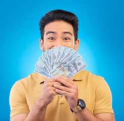 Image showing Cash, fan and man with wow face isolated on blue, studio background for winning, money surprise or financial success. Lottery, finance secret and asian person winning, bonus and cashback in portrait