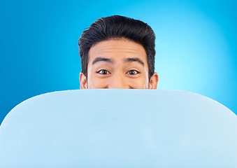 Image showing Board, peek and portrait of a man in a studio with mockup space for marketing, advertising or promotion. Excited, hide and male model with a poster mock up for design isolated by a blue background.