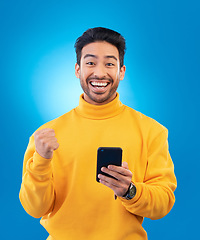 Image showing Winner, excited and portrait of Asian man with phone in studio for online bonus, competition and prize. Success, smartphone and male person celebrate on blue background for promotion, winning or news