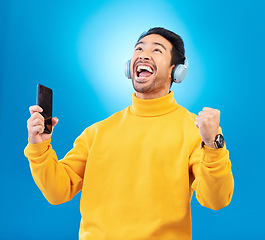 Image showing Celebration, man with smartphone and headphones against blue background listening to radio. Music or podcast, success or achievement and male person with cellphone happy for playlist or streaming