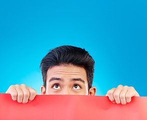 Image showing Eyes, poster and mockup with a man hiding in studio isolated on a blue background for advertising information. Space, sign and a male brand ambassador showing an empty placard for a marketing logo