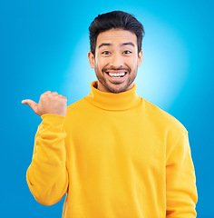 Image showing Portrait, man and pointing to advertising space in studio, blue background and mockup of deal, promotion or news. Happy asian, male model and presentation of announcement, information or opportunity