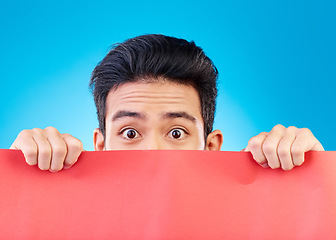 Image showing Portrait, poster and mockup with a man hiding in studio isolated on a blue background for advertising information. Eyes, sign and a male brand ambassador showing empty space for a marketing logo