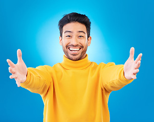 Image showing Portrait, welcome and arms outstretched with a man on a blue background in studio for a friendly hug. Smile, trust and hello with a happy young male person reaching indoor to offer a greeting