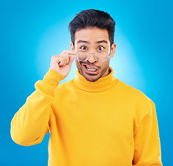 Image showing Portrait, glasses and funny face with a man on a blue background in studio for vision or comedy. Comic, humor and fashion with a silly male person joking in prescription frame lenses or eyewear