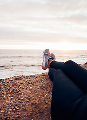 Image showing Fitness, shoes and beach in nature feeling relax with freedom outdoor sitting. Waves, ocean and water with a person and athlete taking a break from training and workout with feet in summer sun