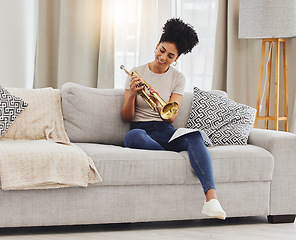 Image showing Happy, woman and learning notes on trumpet in home for music, practice and classic jazz song. Young female person, musician and brass horn instrument on sofa, living room and hobby of musical talent