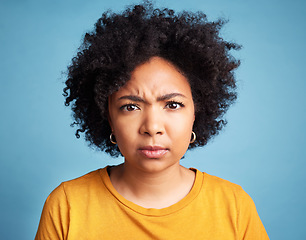 Image showing Portrait, frown and anger with an african woman on a blue background in studio looking mad or serious. Face, bad or negative and an unhappy young female person with an afro feeling frustrated