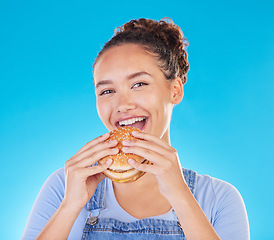 Image showing Burger, smile and woman eating fast food and happy with lunch meal with a smile isolated in a studio blue background. Breakfast, craving and portrait of young female person enjoy snack or sandwich