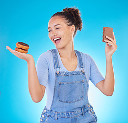 Image showing Food, diet and happy woman with sweets in studio, chocolate and donut for eating plan on blue background. Health, nutrition and choice to lose weight, girl with smile and freedom for sugar or dessert