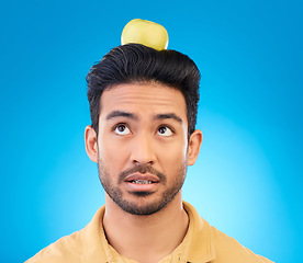Image showing Man, thinking or balance apple on head in studio isolated on a blue background. Confused, fruit or Asian person with food for healthy diet, nutrition or vitamin c for wellness, benefits or vegan idea