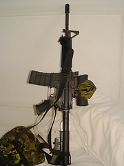 Image showing War, camouflage and a rifle on a bed in the home of a soldier ready for conflict, battle or fighting. Army, military or weapon leaning against a wall in an apartment for self defense or patriotism