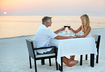 Image showing Mature couple, beach and dinner in sunset for romantic outdoor date, valentines day or anniversary. Senior man and woman with wine, cheers or celebration on table in relax or romance by ocean coast