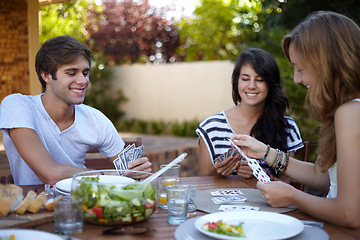 Image showing Friends, card game and food in backyard for lunch and discussion with a smile and fun. Salad, laughing and young people outdoor of a home with communication and funny joke together with a meal