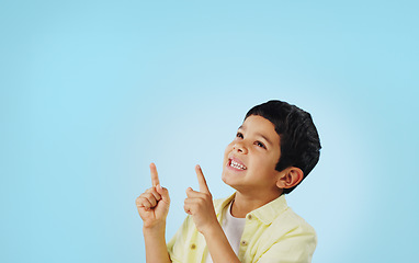 Image showing Kid, boy and smile while pointing in studio on blue background with mockup for announcement, offer or deal. Youth, happy and excited about notification on social media, online or digital marketing