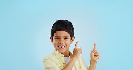 Image showing Kid, boy and smile while pointing in studio on blue background with mockup for announcement, offer or deal. Youth, happy and excited about notification on social media, online or digital marketing