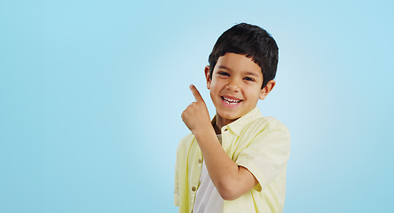 Image showing Boy, smile and pointing with excitement in studio on blue background in mockup for opportunity, deal or alert. Youth, kid and happy with offer, discount or announcement on social media for consumers