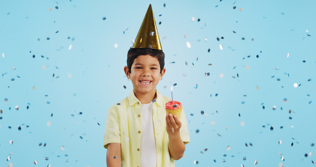 Image showing Happy birthday, child and portrait with confetti in party with cupcake, hat and happiness in studio blue background. Congratulations, kid and boy with cake, glitter and smile on face for magic event