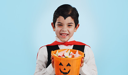 Image showing Halloween, basket and portrait of child with sweets or candy isolated in a studio blue background and happy. Holiday, laughing and kid in vampire costume for celebration in fantasy festival of horror