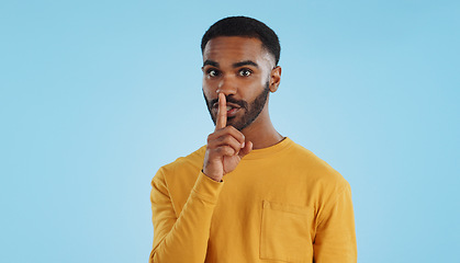 Image showing Secret, face and man with finger on lips in studio for quiet, privacy or hush news on blue background. Whisper, drama and portrait of guy model with confidential hand emoji for gossip or announcement