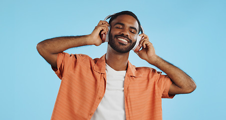 Image showing Black man, headphones and dancing to music with happiness and energy in studio on blue background. Techno, rave and fun with audio streaming, dancer is excited with smile and wireless technology