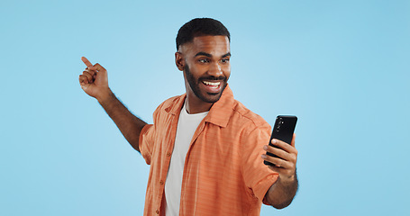 Image showing Happy, face and man with phone in hand pointing in studio for news, smartphone presentation or platform offer on blue background. Smile, portrait and male model show promo, launch or space for coming