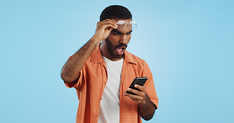 Image showing Man, smartphone and surprise announcement with shock, facial expression and drama online on blue background. Wow, reaction to news on social media and communication, mobile app and alarm in studio