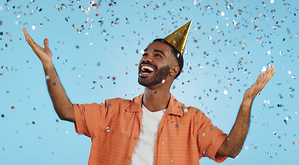 Image showing Man, birthday party hat and confetti in studio, smile or surprise for celebration by blue background. Person, event and excited with silver glitter, achievement or happy for winning with wow for goal