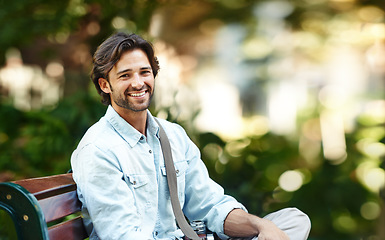 Image showing Nature, relax and portrait of a man on a park bench for a break, morning commute or travel. Smile, summer and a young person or tourist in a public garden for tourism, sightseeing or a vacation