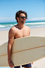 Image showing Man, surfing and happy on vacation with sunglasses by the beach and sea for fitness and water sport with smile. Confidence, male person and surfboard for workout and training by ocean with freedom