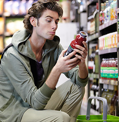 Image showing Man, label and product in supermarket for decision, consider or grocery shopping nutrition choice. Male person, thinking and bottle shelf store search or reading price, diet value or buy organic