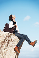 Image showing Thinking, cliff and happy business man for freedom, opportunity and career success in nature. Professional, sitting and corporate worker on rocks edge for holiday, relaxing and break with blue sky