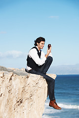 Image showing Cliff, edge and man with a phone at the ocean, beach or happy connection on vacation, travel or social media. Businessman, contact and edgy chat with cellphone, communication or internet above sea