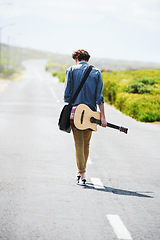 Image showing Musician, walking and man with a guitar on a road trip, journey or tour in the countryside on highway. Guitarist, travel or back of guy trekking on street or asphalt in a green and rural landscape