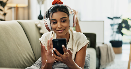 Image showing Phone, music headphones and happy woman on sofa in home, listening to audio or video app to relax. Smartphone, sound and Indian person on radio or typing on social media in living room on mobile tech